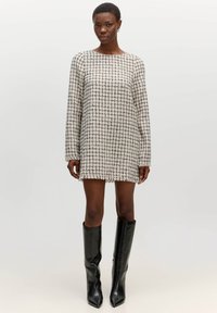 Gestreepte mini-jurk met lange mouwen, gemaakt van gestructureerde stof in crème en zwart. Randen zijn iets rafelig. Gecombineerd met knielange zwarte laarzen.