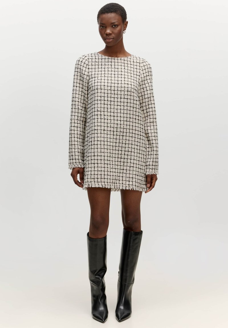 Gestreepte mini-jurk met lange mouwen, gemaakt van gestructureerde stof in crème en zwart. Randen zijn iets rafelig. Gecombineerd met knielange zwarte laarzen.