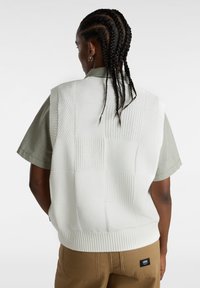 Hvid strikket vest med et ternet m�ønster, der har forskellige teksturer; båret over en grøn t-shirt med korte ærmer i en afslappet pasform.