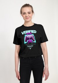 Černé tričko s živým grafickým textem "OVĚŘENO" a barevným designem herního ovladače, který obsahuje fialové akcenty a tučný písmový design.