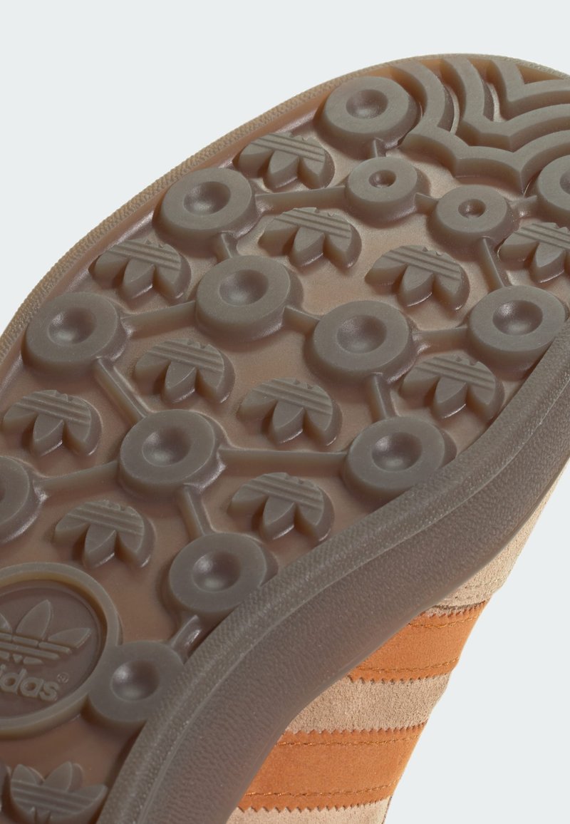 Podeszwa pomarańczowego i beżowego sneaker'a o teksturowanej gumowej powierzchni, z okrągłymi i liściastymi wzorami oraz logo Adidas.