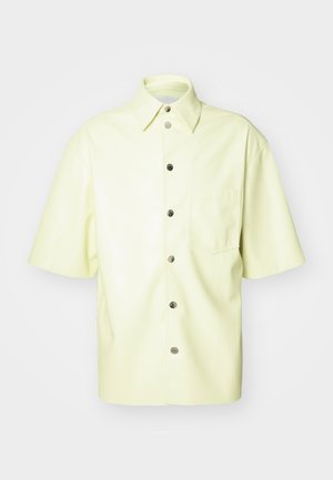 Lühikeste varrukatega särgid heledast kollasest kunstnahast. Omab esitaskut, nööpide sulgemist ja klassikalist kraed. Sile ja läikiv tekstuur.