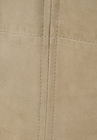Beiger Wildlederstoff mit einer glatten Textur und einer zentralen Naht. Die Oberfläche zeigt subtile Variationen in Farbton und Tiefe.