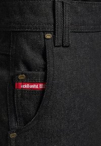 Mustad denim püksid siledaga tekstuuriga, millel on peidetud tasku ja punane logo silt "eckō unlt." vöökoht. Kuldsetest detailidest aksessuaarid.