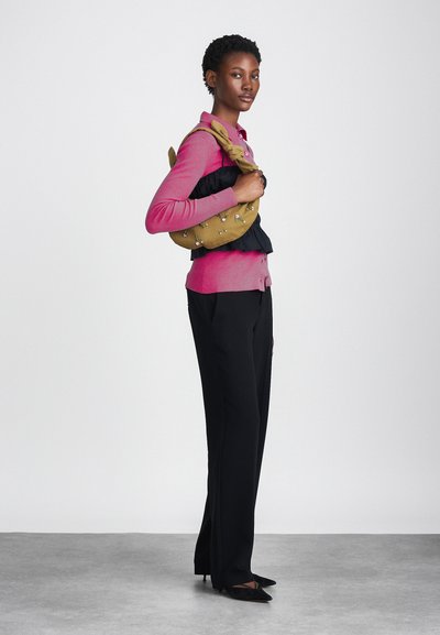 Roosa sobiv kardigan nööpidega, must kihiline pluus, mustad kohandatud püksid ja tekstuurne sinepikollane käekott kaunistustega.