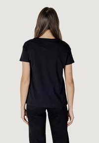 Czarny bawełniany t-shirt z krótkimi rękawami i okrągłym dekoltem. Charakteryzuje się prostym wzornictwem bez wzorów czy akcentów. Pokazano widok z tyłu.