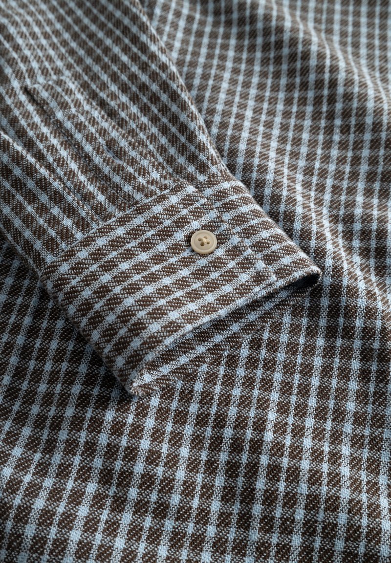 Brown and light blue checkered fabric with a textured surface, featuring a buttoned cuff and visible stitching details.