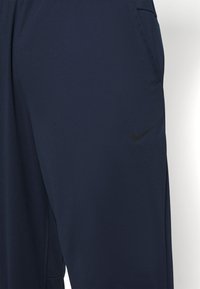 Navy blue athletic pants made of lightweight fabric, featuring a subtle Nike logo in black on the thigh and side pockets for convenience.
