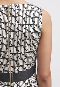 Robe noir et blanc avec un motif d'oiseaux et de lignes, en tissu lisse, bustier ajusté et une ceinture noire contrastante. Fermeture éclair dorée au dos.