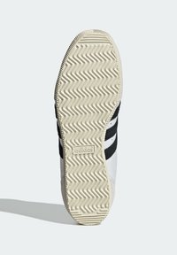 Bílá podešev atletické boty s cikcak vzorem podrážky, s černými pruhy a značkovým detailem na boku.
