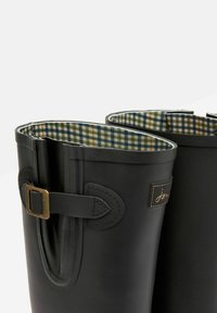 Črne gumijaste škornje za dež, obložene s karirasto zeleno-modro tekstilno podlogo, z dekorativno sponko in šivanimi detajli na zunanjosti.