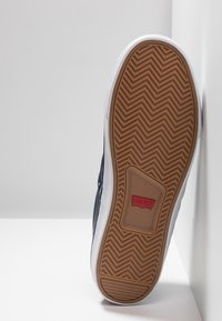 Baskets Levi's avec une semelle extérieure en caoutchouc gomme texturé, une semelle intermédiaire blanche et une tige en toile marine. Présentent un détail de logo rouge proéminent.
