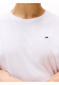 White cotton t-shirt with a crew neck and short sleeves, featuring a small embroidered logo in red, white, and blue on the chest.