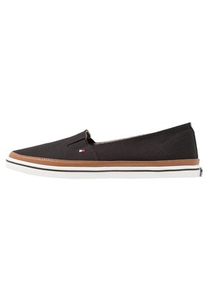 Scarpe slip-on nere in tela con una fascia accentata marrone, suola bianca e dettagli con piccolo logo. Design elegante e profilo piatto con cuciture minime.