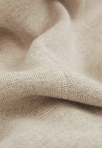 Vaalean beige neulekangas, jossa on pehmeä rakenne, ribattuja yksityiskohtia ja sileä pinta, esittelee eroja langan paksuudessa.