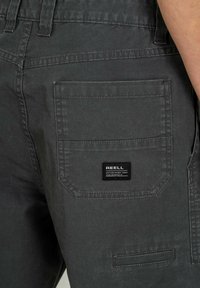 Gray cargo shorts made from durable fabric, featuring a large side pocket and a small brand label with text on the back.