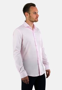 Lichtroze overhemd met lange mouwen en een kraag met knopen, gemaakt van gladde stof, passend ontwerp, gedragen met een donkere broek.