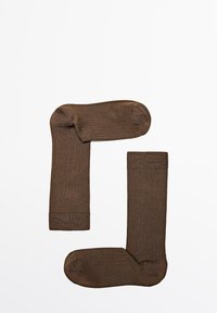 Et par ensfarvede brune ankelstrømper lagt fladt på en hvid baggrund, hvor den ene er justeret vertikalt og den anden horisontalt.