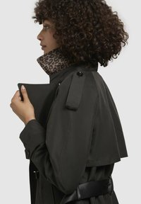 Trench coat de un verde închis cu un guler cu imprimeu de leopard, având un talie cu brâu și epoleți cu nasturi. Textură netedă și design ajustat.