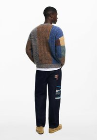 Pulover tricotat multicolor cu textură patchwork; pătrate albastre, maronii și galbene. Asortat cu blugi negri din denim, decorati cu un patch peisaj.