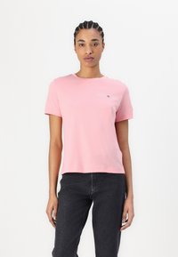 Lyserød bomulds t-shirt med rund halsudskæring. Har et lille trykt logo på brystet. Korte ærmer, løs pasform, glat tekstur.