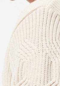 Cream knitted sweater featuring a textured, cable knit pattern with ribbed collar and cuffs, made from soft yarn material.