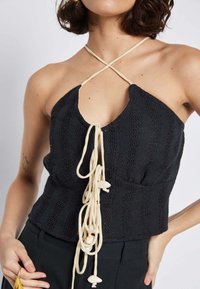 Top halter nero con texture e scollatura profonda, dotato di lacci color crema e perline decorative, creando una silhouette strutturata.