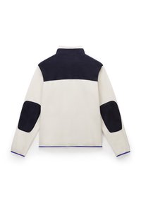 Giacca in pile con corpo crema, spalle blu navy e toppe sui gomiti. Presenta un colletto alto e un bordo blu a contrasto lungo l'orlo.