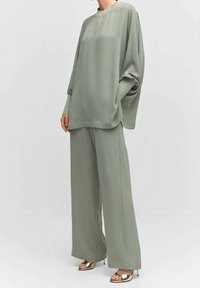 Pantalons larges vert clair texturés associés à un haut ample assorti ; il possède des manches longues et un col rond. Sandales à talons dorés.