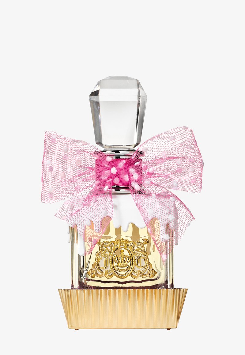 Flacon de parfum transparent avec emblème doré, bouchon clair facetté et grand nœud en mesh rose à pois attaché autour du cou.