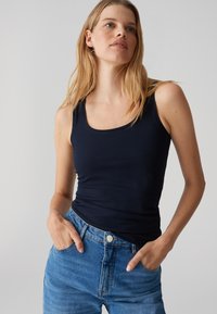 Canotta blu navy con scollatura a forma di uovo e design aderente. Indossata con jeans di denim blu chiaro con tasche frontali.