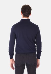 Maglione blu navy a maniche lunghe con colletto e polsini a costine, abbinato a pantaloni scuri. Il tessuto del maglione appare liscio e aderente.