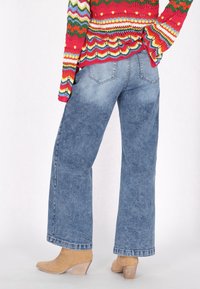 Jeans de pierna ancha de color azul claro con una textura de denim suave, con dos bolsillos traseros y un ajuste casual, combinados con botas de tobillo de tacón color marrón claro.