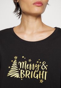 T-shirt noir à manches courtes avec un texte doré "Joyeux et Éclatant" accompagné de graphiques stylisés d'un sapin de Noël et d'une étoile. Texture de tissu lisse.