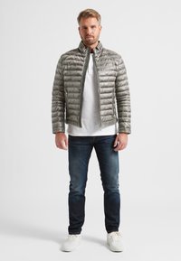 Hellgraue Daunenjacke mit gestepptem Design, Frontreißverschluss und Stehkragen. Kombiniert mit dunkelblauen Denim-Jeans und weißen Sneakers.