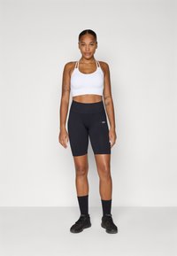 Witte sportbh met een multi-band ontwerp, gecombineerd met hoge zwarte fietsshorts. Beide kledingstukken hebben een gladde, rekbare textuur.