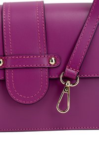 Lila synthetische Handtasche mit Klappenverschluss, goldenen Beschlägen, kontrastierenden Nähten und einem abnehmbaren Tragegurt. Glatte Oberfläche, keine sichtbaren Muster.