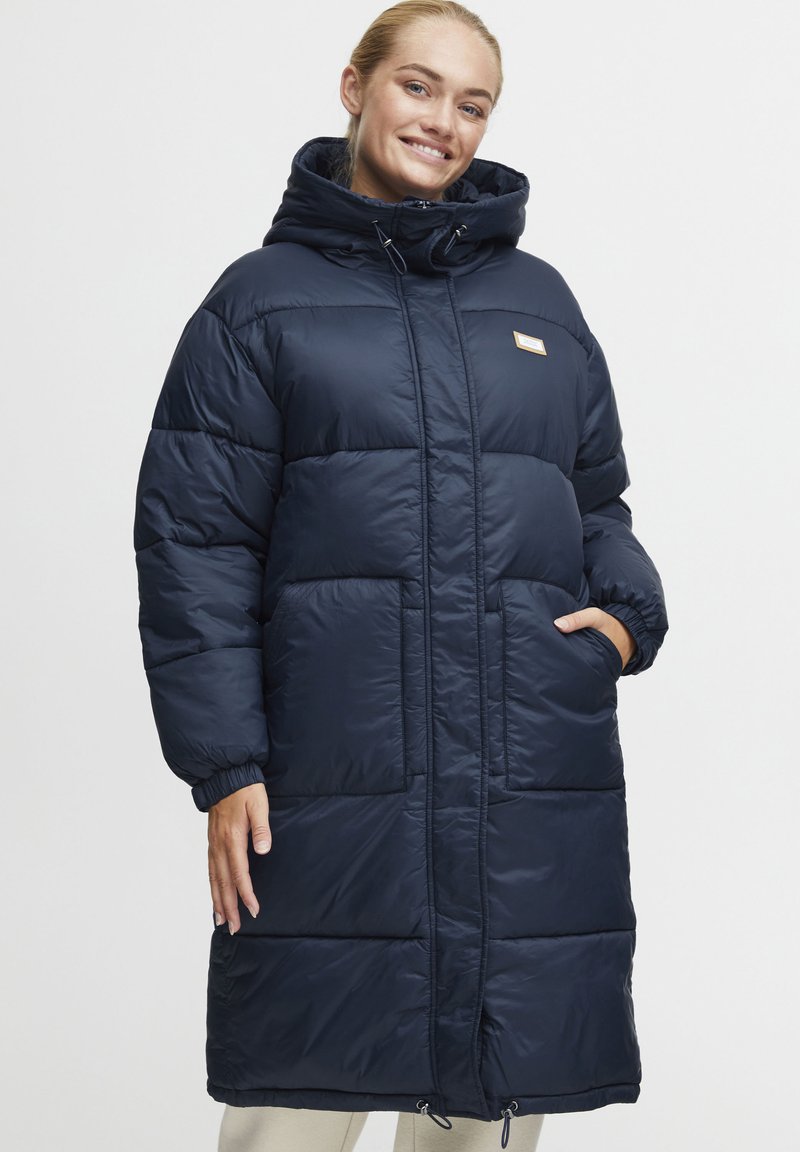 Cappotto imbottito blu navy con cappuccio, caratterizzato da ampi pannelli a trapunta, tasche laterali e cordini regolabili all'orlo e al collo.