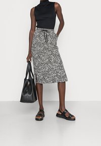 Czarny top bez rękawów, spódnica do kolan z abstrakcyjnym czarno-białym wzorem, czarna skórzana torebka oraz czarne sandały na masywnej podeszwie.