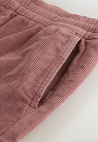 Primer plano de pantalones de pana rosa con cintura elástica y un bolsillo lateral.