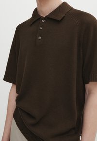 Brązowa dzianinowa koszulka polo z kołnierzykiem, krótkimi rękawami, trzyguzikowym rozpięciem oraz prążkowanymi ściągaczami zapewniającymi teksturę i strukturę.