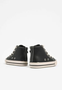 Sorte højhælede sneakers lavet af tekstureret materiale, med lyse snørebånd, hvide syninger og gummisåler med sorte striber.