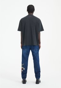 Camiseta de algodón negra, de corte holgado, con un sutil estampado gráfico en la parte trasera. Combinada con jeans de mezclilla azul, adornados con bordado lateral.