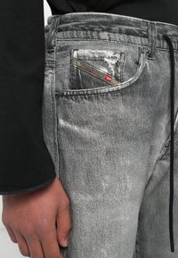 Τζιν γκρι με διακριτική φθορά. Διαθέτει μικρή ετικέτα με λογότυπο στην πίσω τσέπη και κορδόνι στη μέση.