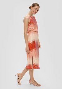 Paillette-jurk in gradiënttinten van roze en rood, mouwloos, met een aangesloten taille en een zijspleet, gecombineerd met lichtroze sandalen met bandjes.