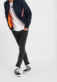 Navy bomber jacket with orange lining, white t-shirt, black slim-fit jeans, and black sneakers with white accents. Keychain detail on jacket.