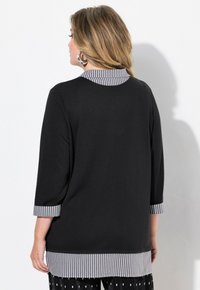 Maglietta nera con maniche a tre quarti, caratterizzata da un colletto e polsini a righe. Strisce orizzontali all'orlo con una texture liscia.