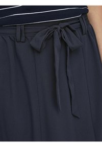 Tissu bleu marine foncé avec une finition texturée, comportant un nœud attaché à la taille et des passants de ceinture, conçu avec des plis pour un look fluide.