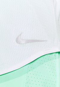 Camiseta deportiva Nike en menta clara y blanca. Presenta un tejido ligero y transpirable con el logo en plata y textura de malla.