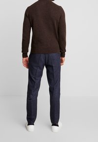 Brun stickad tröja, mörkblå texturerade byxor, vita sneakers. Avslappnad passform, ribbade manschetter och fåll, synliga sömmar på byxorna.